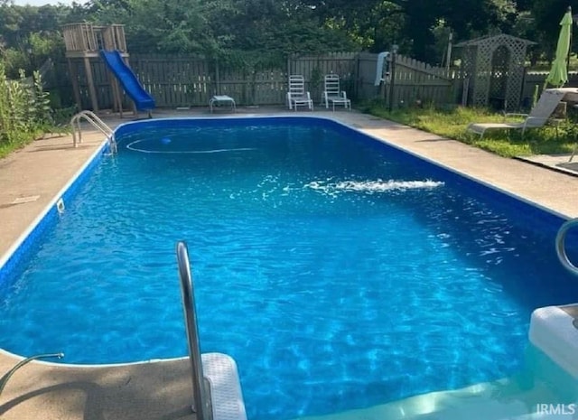 view of pool featuring a fenced in pool, fence, a water slide, and a playground