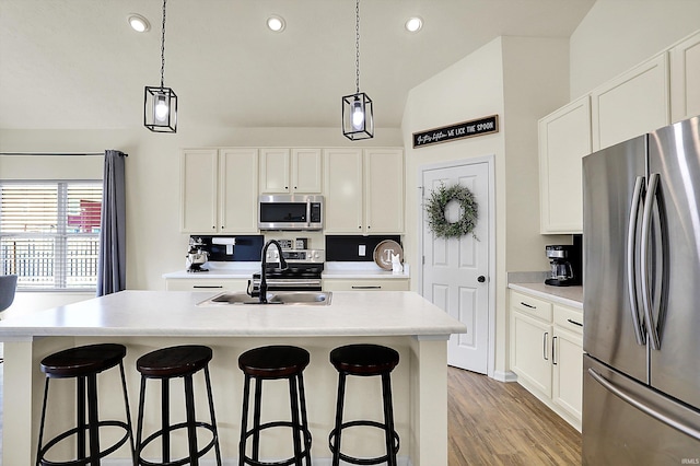 kitchen with a breakfast bar area, a center island with sink, a sink, white cabinets, and appliances with stainless steel finishes