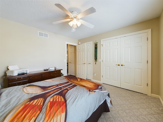 bedroom featuring visible vents, multiple closets, a textured ceiling, carpet floors, and ceiling fan