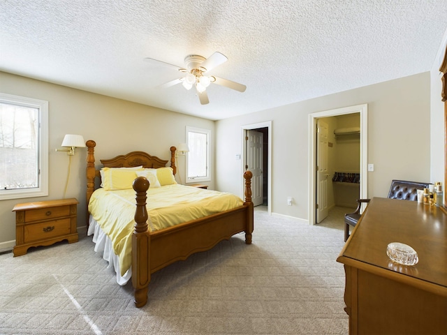 bedroom featuring a walk in closet, baseboards, ceiling fan, light carpet, and a textured ceiling