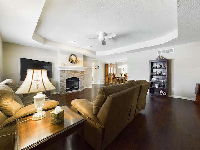 living area with wood finished floors, visible vents, a textured ceiling, a raised ceiling, and ceiling fan with notable chandelier