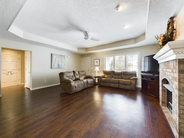 living room with baseboards, a fireplace, ceiling fan, dark wood-type flooring, and a raised ceiling