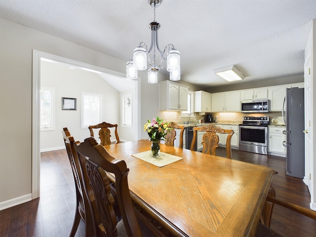 dining area featuring dark wood finished floors, a textured ceiling, baseboards, and an inviting chandelier