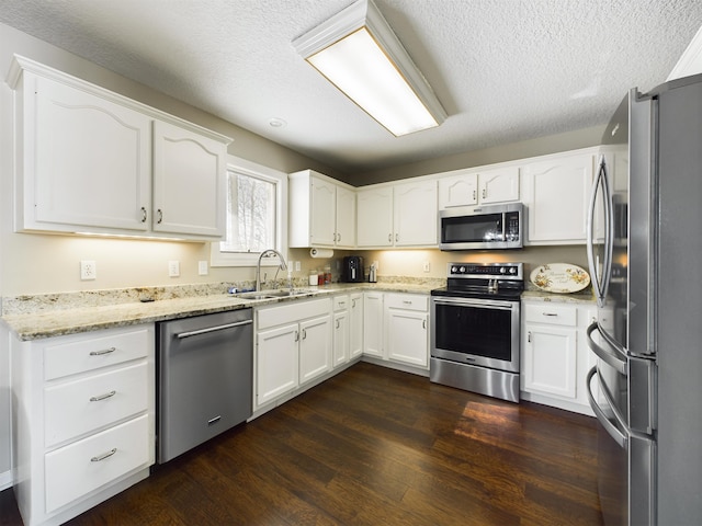 kitchen featuring light stone countertops, a sink, dark wood-type flooring, appliances with stainless steel finishes, and white cabinetry