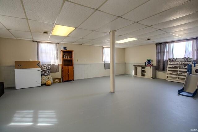 basement with wainscoting, a drop ceiling, and a healthy amount of sunlight