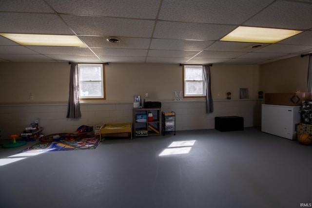 basement with a drop ceiling, visible vents, and concrete block wall