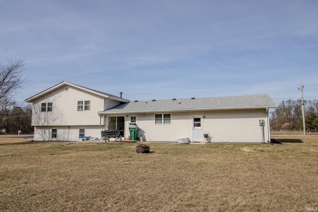 rear view of house featuring a lawn, roof with shingles, and an outdoor fire pit