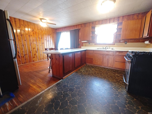 kitchen with wooden walls, ceiling fan, a peninsula, freestanding refrigerator, and stainless steel gas stove