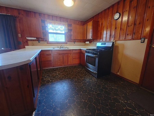 kitchen with a sink, stone finish flooring, brown cabinetry, light countertops, and gas range