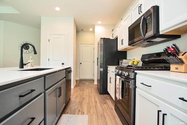 kitchen with a sink, stainless steel appliances, light wood-style floors, white cabinets, and light countertops