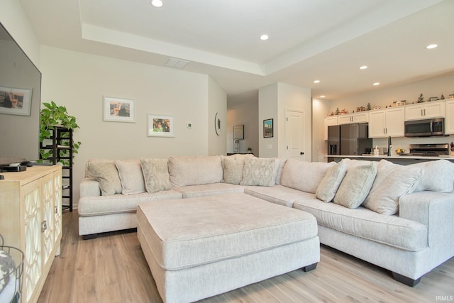 living area featuring recessed lighting, a raised ceiling, and light wood-style flooring