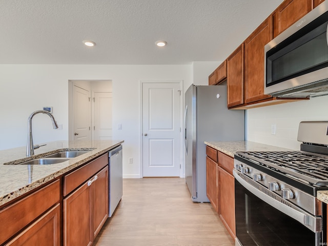 kitchen featuring light stone countertops, brown cabinets, a sink, appliances with stainless steel finishes, and tasteful backsplash