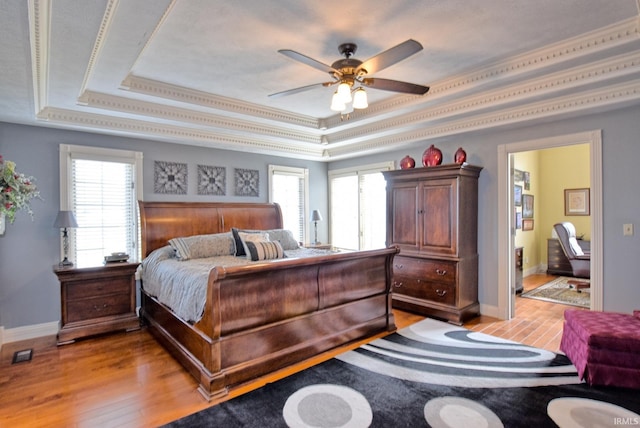 bedroom featuring a tray ceiling, multiple windows, and light wood-type flooring