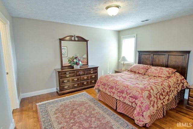 bedroom with visible vents, wood finished floors, baseboards, and a textured ceiling