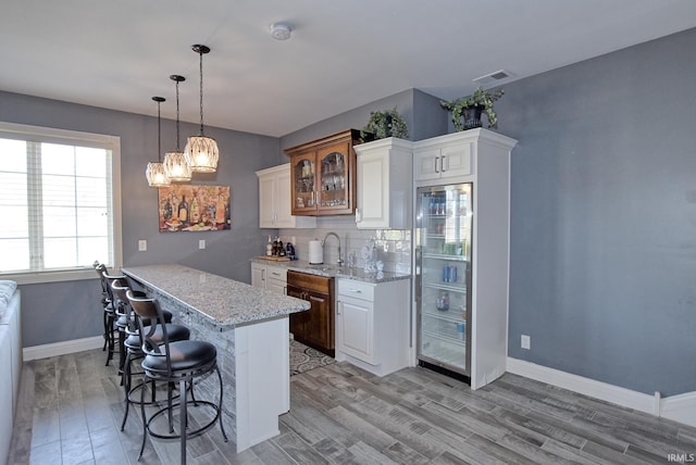 kitchen with a breakfast bar area, visible vents, a sink, glass insert cabinets, and light wood-type flooring