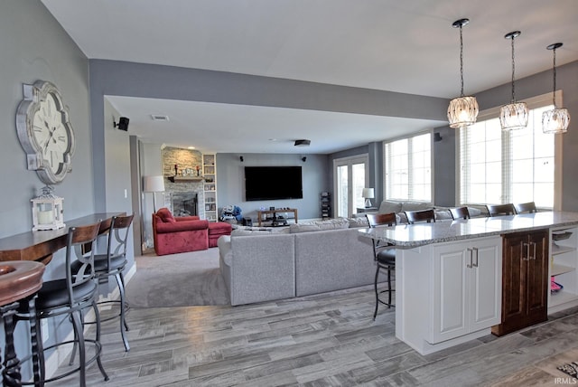 living area with a stone fireplace, visible vents, and light wood-style floors