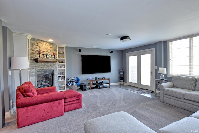 living area with baseboards, carpet, a stone fireplace, and built in shelves