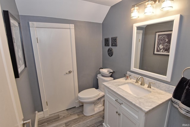 bathroom with toilet, wood finished floors, vanity, and vaulted ceiling