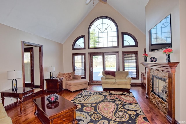 living area featuring a fireplace, high vaulted ceiling, dark wood-type flooring, and ceiling fan