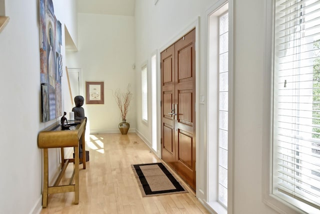 foyer entrance featuring light wood-type flooring, baseboards, and a towering ceiling