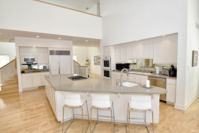 kitchen with a sink, a large island, light wood-style floors, appliances with stainless steel finishes, and a kitchen bar