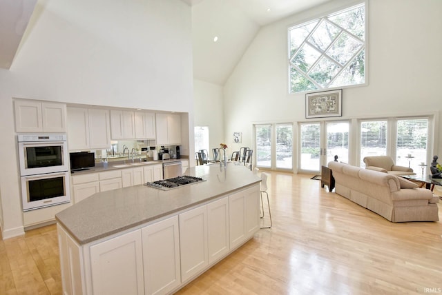 kitchen with light wood-type flooring, open floor plan, stainless steel appliances, white cabinets, and light countertops