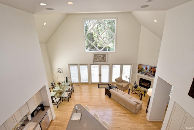 living area with light wood finished floors, plenty of natural light, a fireplace, and high vaulted ceiling