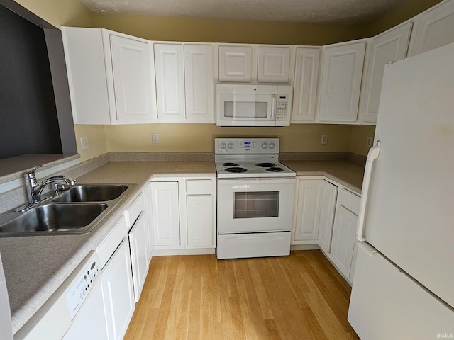 kitchen featuring white appliances, white cabinets, light wood-type flooring, and a sink