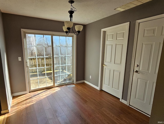 unfurnished dining area featuring visible vents, baseboards, dark wood-style floors, a notable chandelier, and a textured ceiling