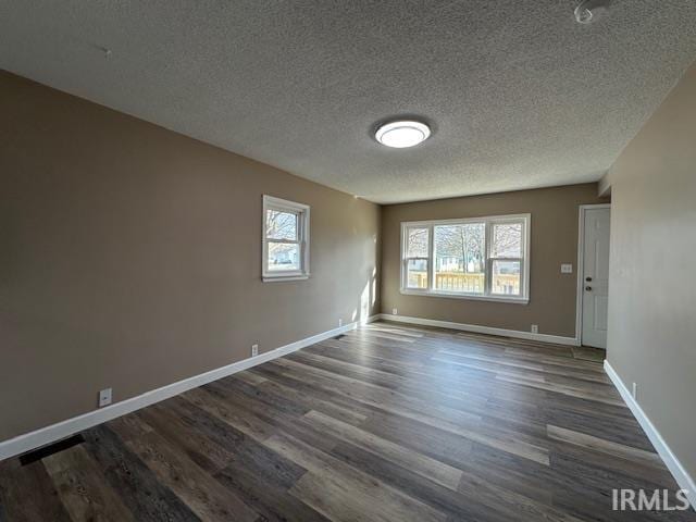 spare room featuring baseboards, dark wood-type flooring, and a healthy amount of sunlight