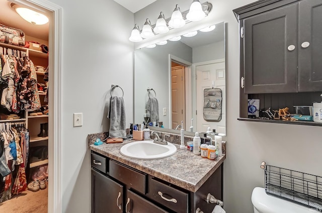 bathroom with a walk in closet, toilet, and vanity