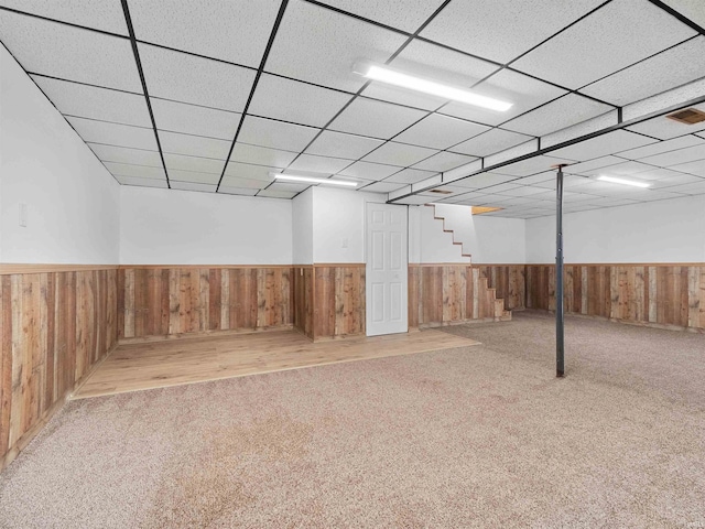 finished basement with stairway, wooden walls, carpet, a paneled ceiling, and wainscoting