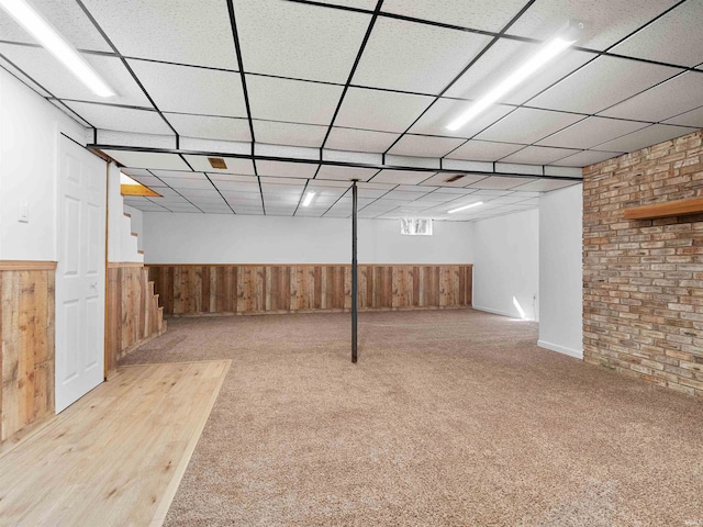 basement with a drop ceiling, wooden walls, and wainscoting