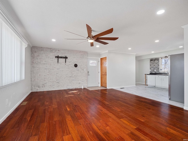 unfurnished living room with wood finished floors, recessed lighting, brick wall, baseboards, and ceiling fan