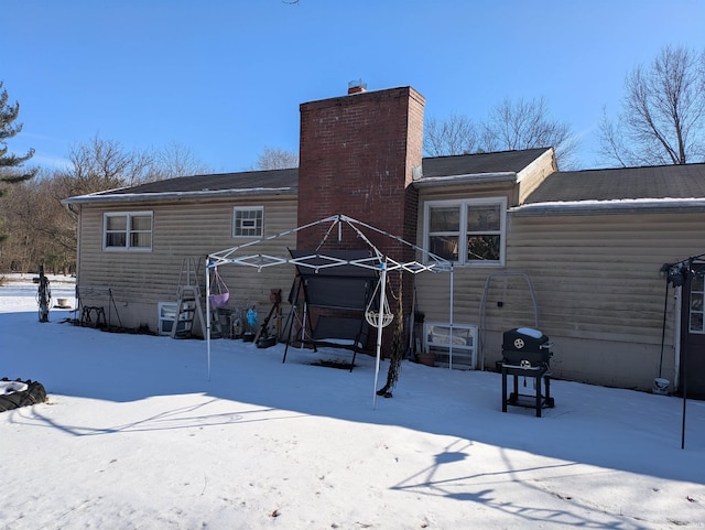 snow covered rear of property featuring a chimney