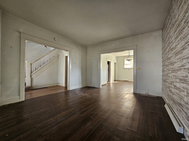 unfurnished room featuring stairway, a baseboard heating unit, baseboards, and wood finished floors