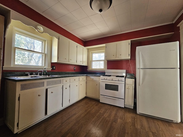 kitchen featuring dark countertops, dark wood finished floors, white cabinets, white appliances, and a sink