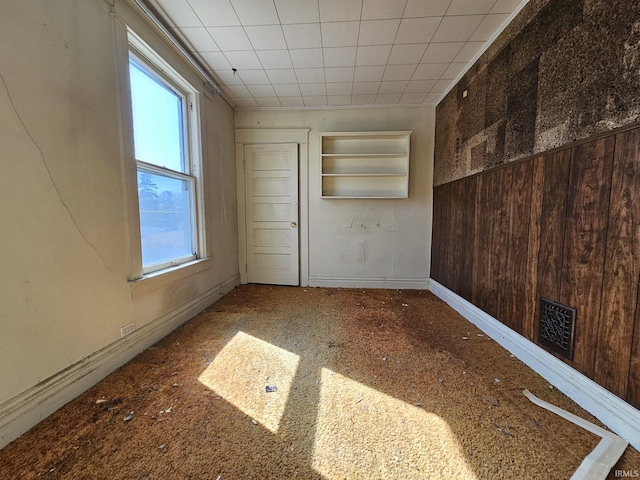 empty room featuring visible vents, baseboards, and wooden walls