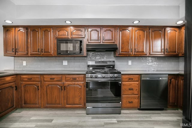 kitchen featuring under cabinet range hood, decorative backsplash, light wood finished floors, and appliances with stainless steel finishes