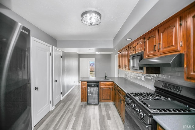 kitchen with beverage cooler, under cabinet range hood, range with gas stovetop, freestanding refrigerator, and a peninsula