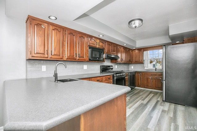 kitchen with a sink, under cabinet range hood, gas range oven, freestanding refrigerator, and black microwave