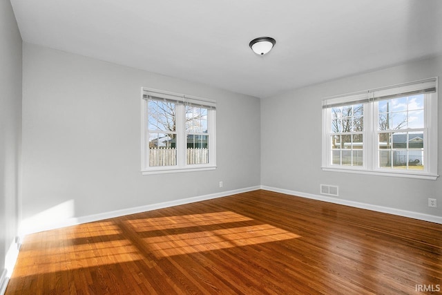 empty room featuring wood finished floors, visible vents, and baseboards