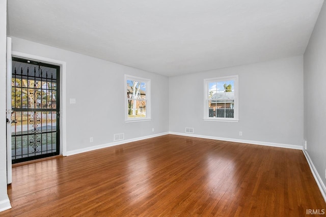 spare room featuring baseboards, a healthy amount of sunlight, and wood finished floors