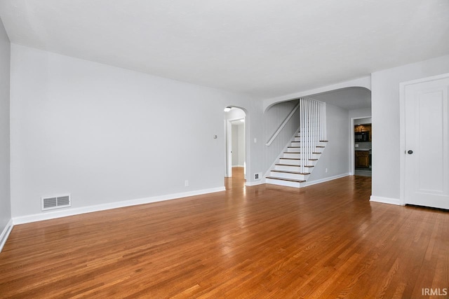 unfurnished living room featuring visible vents, wood finished floors, arched walkways, baseboards, and stairs