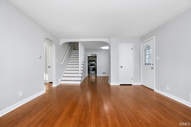 interior space with wood finished floors, visible vents, baseboards, arched walkways, and stairs