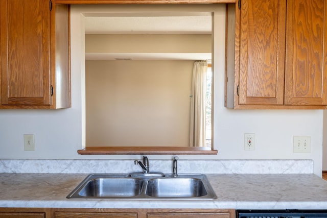 kitchen with dishwashing machine, light countertops, brown cabinets, and a sink