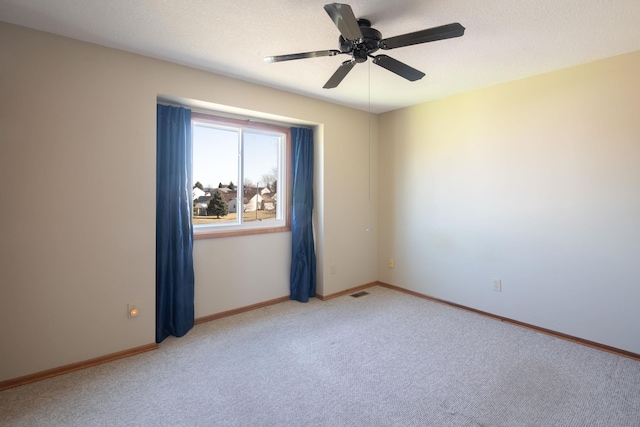 spare room featuring light carpet, a textured ceiling, baseboards, and a ceiling fan