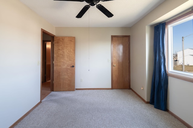 unfurnished bedroom with light colored carpet, a ceiling fan, and baseboards