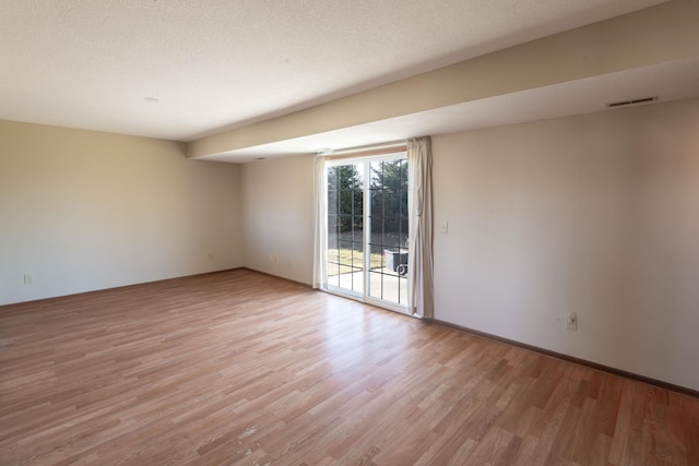 empty room with visible vents, light wood finished floors, and a textured ceiling