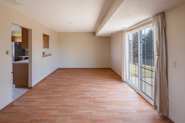 spare room featuring visible vents, plenty of natural light, baseboards, and light wood finished floors